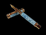 A Red Gold Fountain Pen With Red Gold JOWO #6 Nib. The Body is hand crafted with swirls of silk blue and diamond dust resins giving it the look of clouds before snow.
The Custom Hardware is Intricately Engraved With A Rampant Lion, which adorns both the cap and finial. The Center Band Showcases A Series Of Understated Yet Distinguished Artist Designed “H” . The Fountain pen is sitting on an old manuscript with the body of the pen resting on the cap.