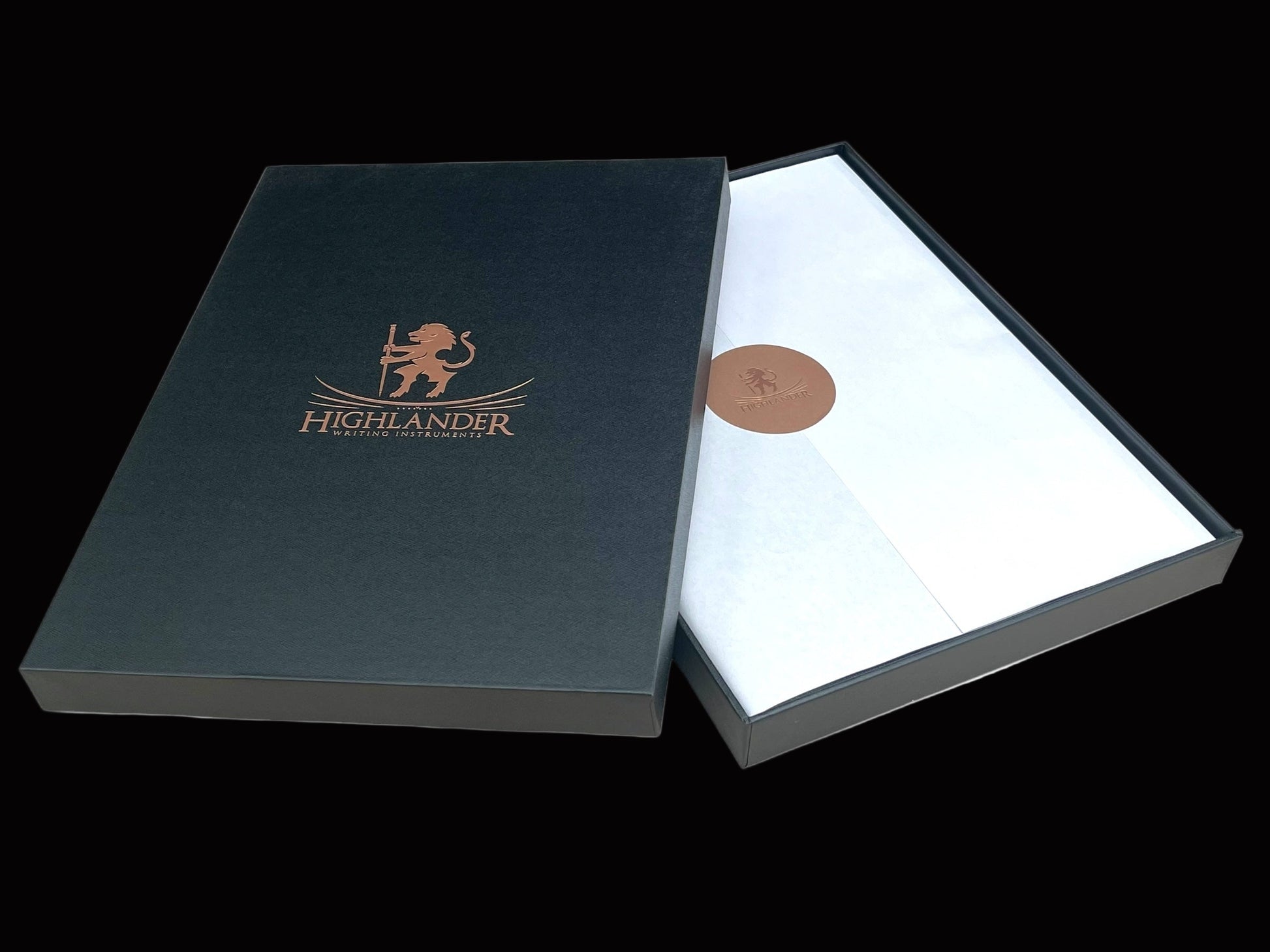 A Black Gift Box With Highlander logo on top in bright red gold copper.  The lid is tilted on the base box showing how the journal is wrapped in tissue and sealed with a Highlander logo sticker