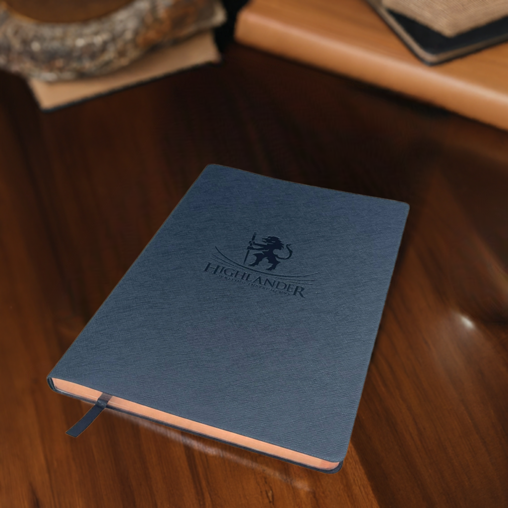 A Highlander Black B5 Journal Sitting on a wood desk with a journal in the background.