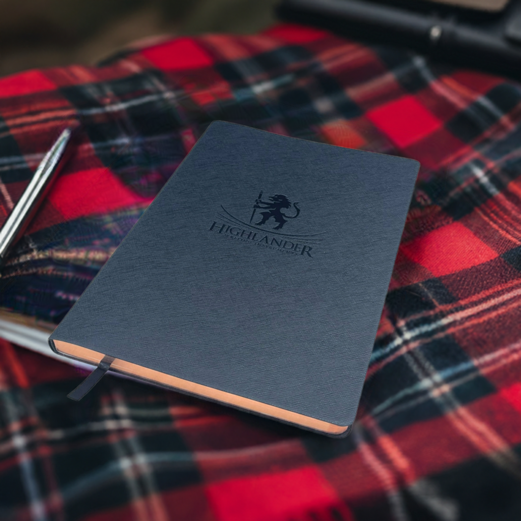 A B5 Black Highlander Journal sitting on a red plaid tartan style throw next to a silver pen.